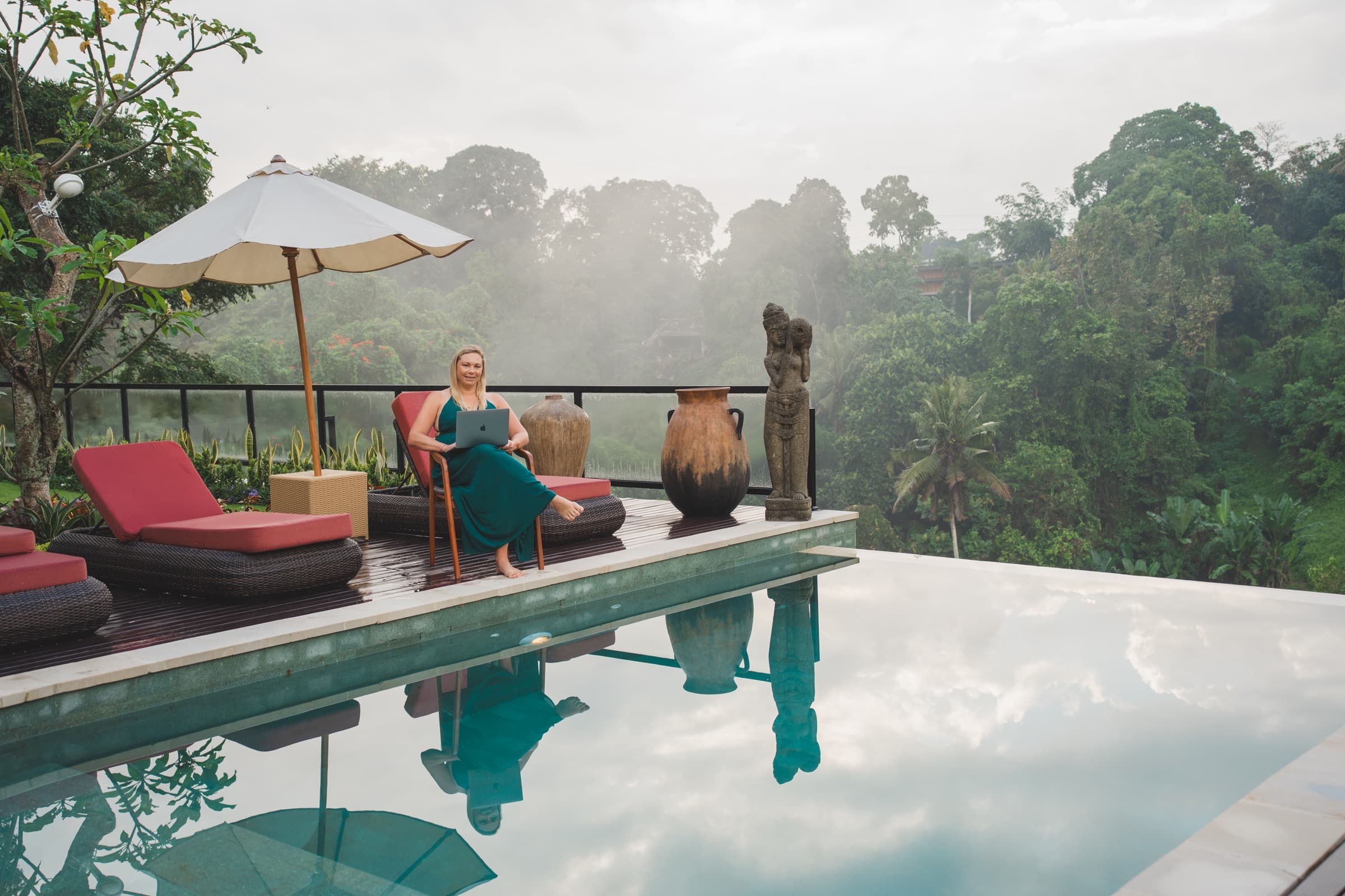 Sheree Ann seated poolside with her laptop, jungle view behind her